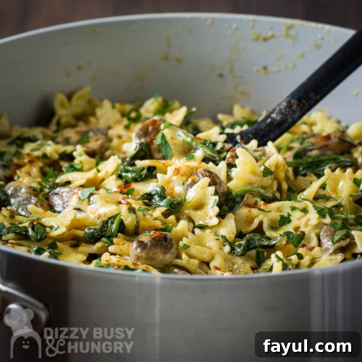 A close-up side shot of the creamy mushroom spinach pasta served in a silver pan with a black serving spoon, highlighting the rich sauce and fresh ingredients.