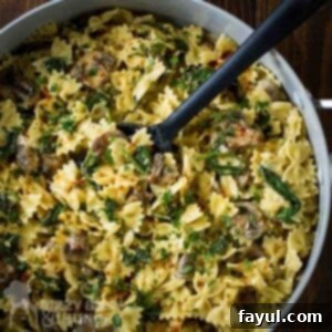 Overhead shot of creamy spinach and mushroom pasta in a large pot with a rubber spoon on a wooden table, ready to serve.