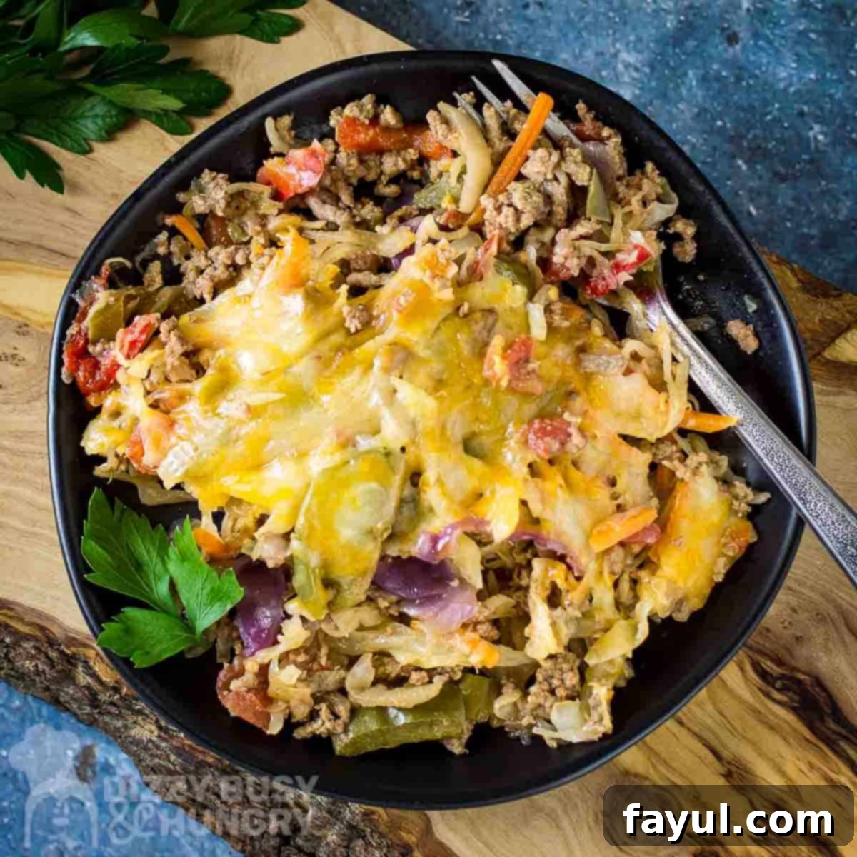 Close up overhead shot of a serving of One-Skillet Stuffed Cabbage Casserole on a black plate with a silver fork on the side, resting on a wooden cutting board on a blue surface with fresh herbs as garnish.