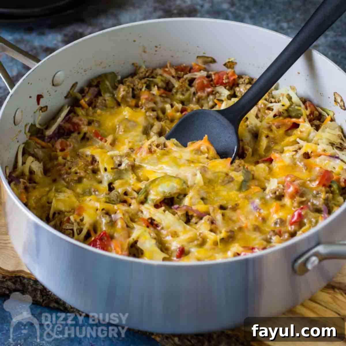 Side angled shot of the finished One-Skillet Stuffed Cabbage Casserole in a large shallow pot with a black spatula, all resting on a wooden surface. A perfect quick and easy weeknight dinner.