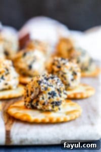 Everything Bagel Cheese Ball Bite on a round cracker on a marble and wood cutting board, ready to be served as an appetizer.