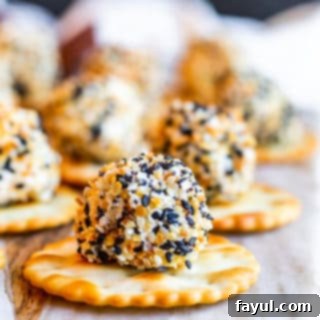 Everything Bagel Cheese Ball Bite on a round cracker on a marble and wood cutting board.