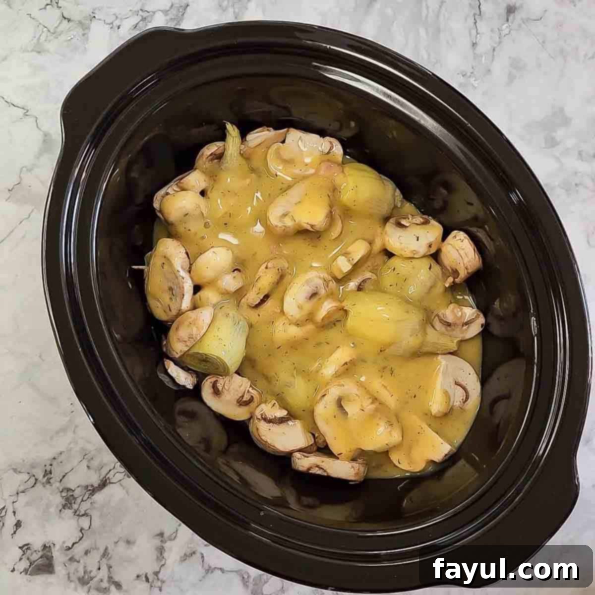 Overhead view of process shot 3 - pouring the prepared soup mixture over mushrooms, artichokes, and chicken in the crock pot.