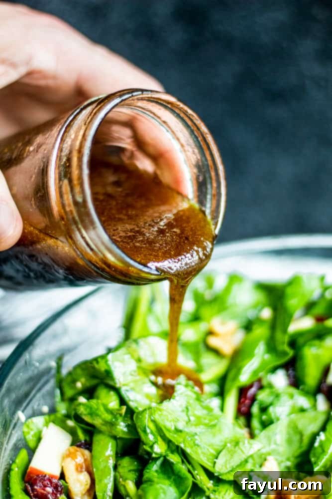 The BEST Healthy Spinach Apple Salad with Homemade Honey Balsamic Vinaigrette. This recipe is perfect for holidays, a side dish or main course. This vegetarian salad is packed with dried cranberries, feta, red onion, apples, and walnuts for the perfect combo. Video included! #salad #healthy #recipe #Food #vegetarianfood #vegetarian Vinaigrette Dressing being poured over spinach salad in a glass bowl.