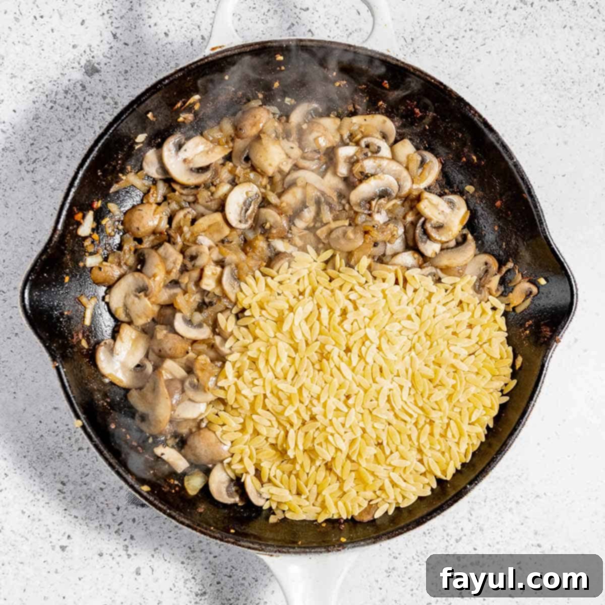 Overhead view of process shot 3 - adding salt, pepper, and dry orzo pasta to the skillet and sautéing for a few more minutes to toast the pasta lightly.