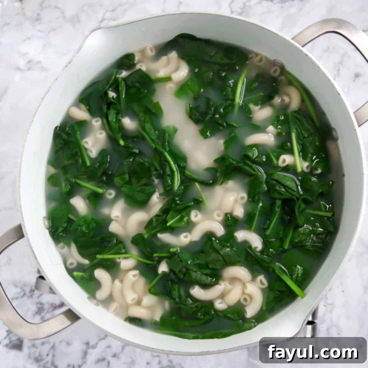 Overhead view of process shot 5 - adding the spinach into the boiling pasta until it is wilted.