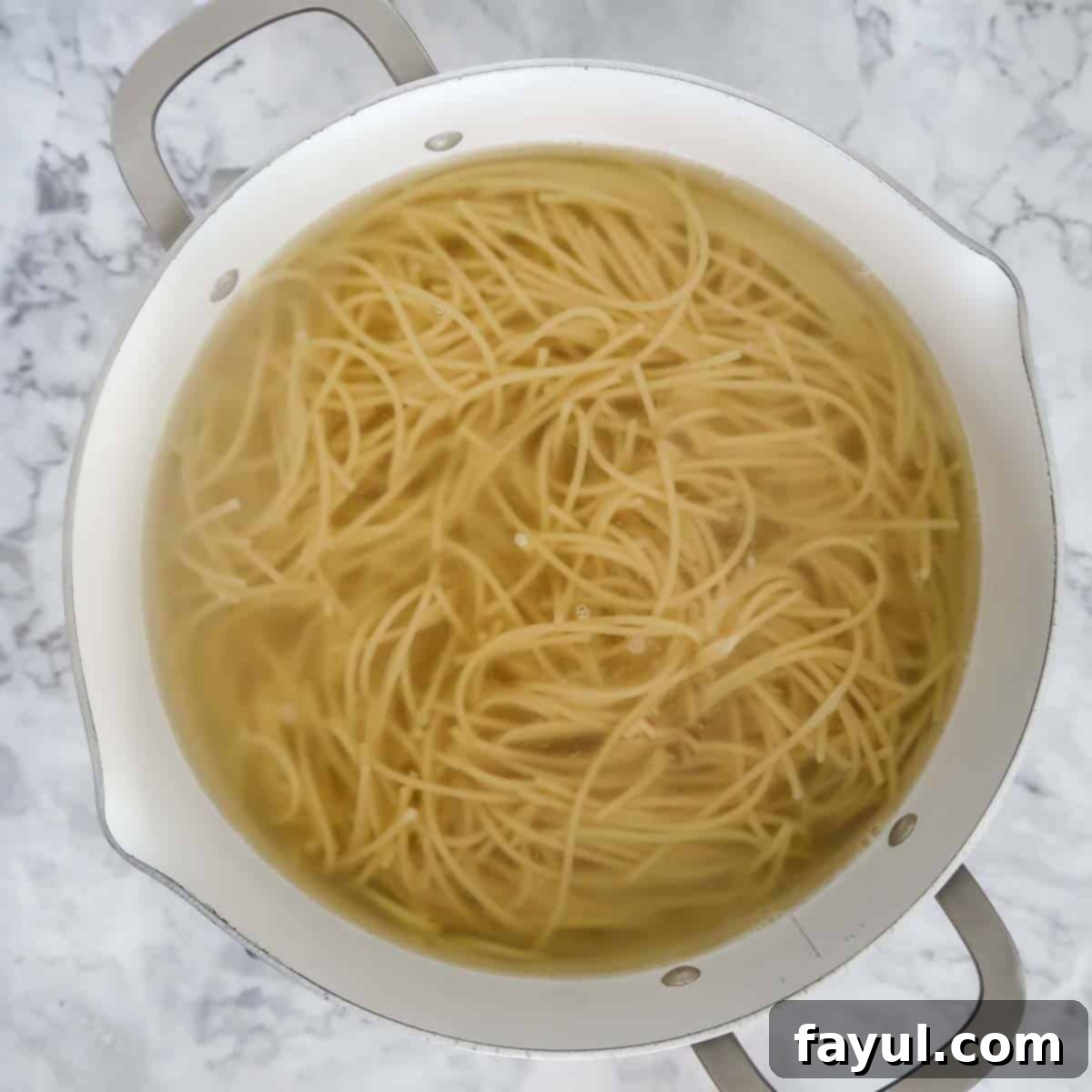 Overhead view of process step 1: thin spaghetti noodles boiling in a large pot of water on a stove.