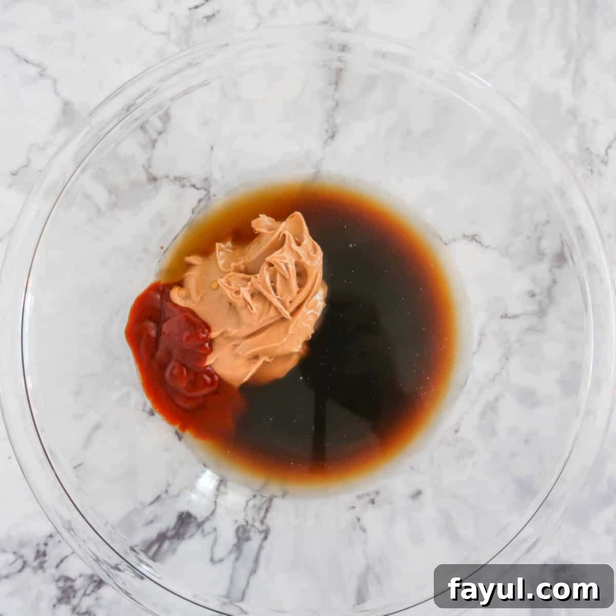 Overhead view of process step 2: various sauce ingredients—peanut butter, honey, chicken broth, sriracha, lime juice, and soy sauce—are combined in a medium glass bowl, ready to be whisked.