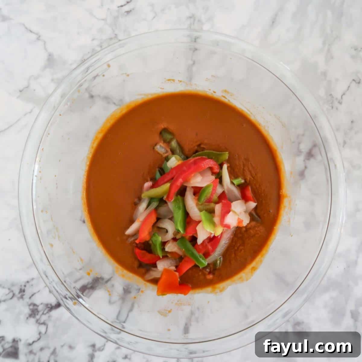Overhead view of process step 4: thawed bell pepper and onion strips being added to the prepared peanut sauce mixture in a glass bowl, ready for mixing.