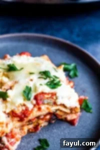 Slice of vegetarian lasagna on a gray plate, showing distinct layers of pasta, sauce, cheese, and vegetables.