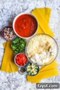 Vegetarian lasagna ingredients displayed on a white counter in various bowls, including chopped vegetables, cheeses, and spices.