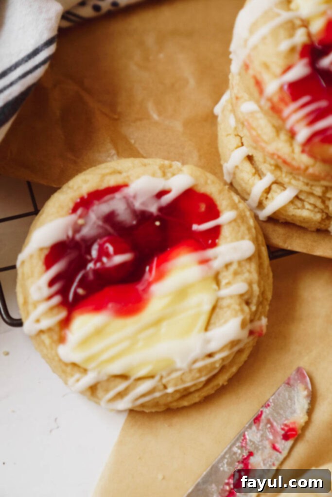 Two cherry cheesecake cookies on a plate with fresh cherries