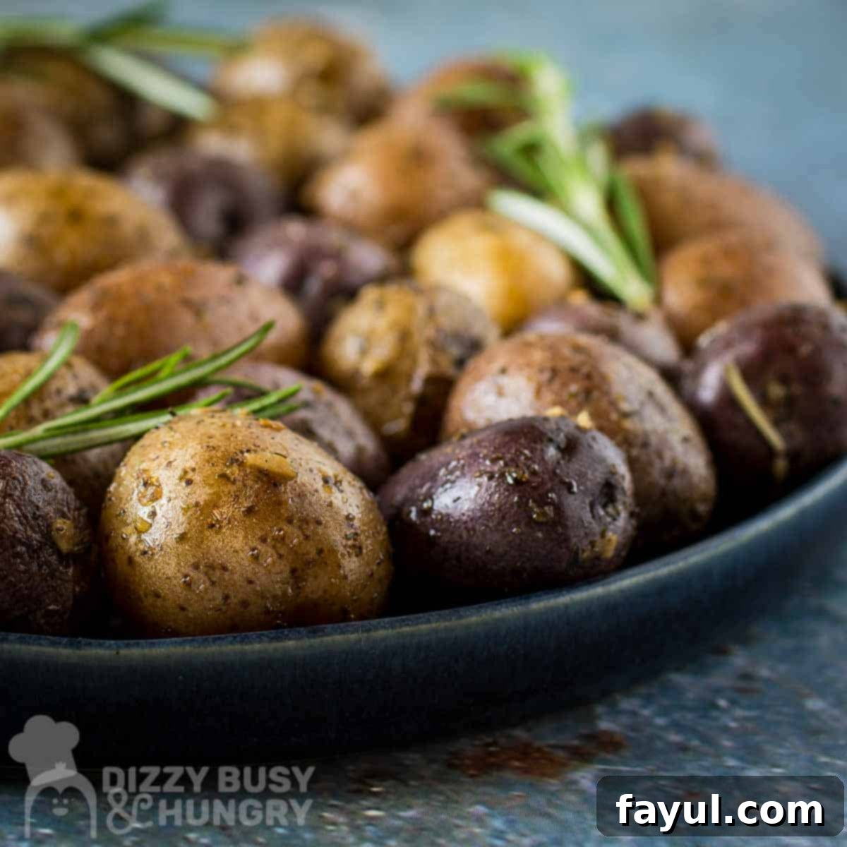 Side close up shot of roasted potatoes garnished with fresh rosemary on a black plate.