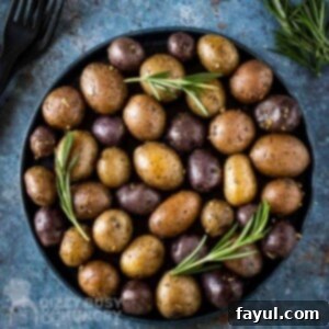 Overhead shot of roasted potatoes garnished with fresh rosemary on a black plate with black silverware and rosemary on the side.
