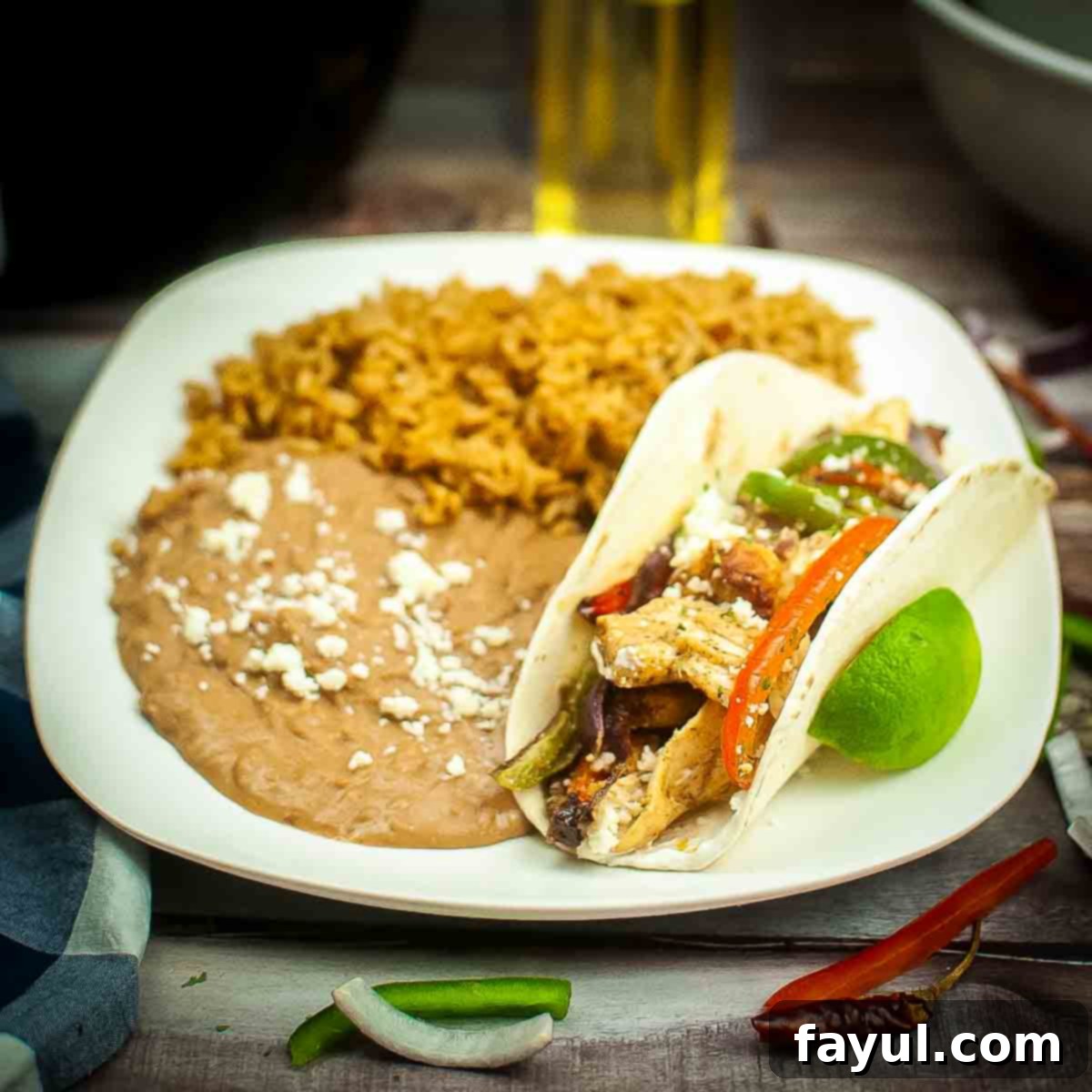 Side angled shot of chicken fajitas sprinkled with cotija cheese with sides of refried beans, rice and a lime wedge on the side.
