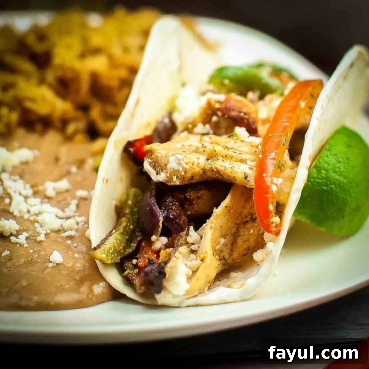 Side close up shot of chicken fajita sprinkled with cotija cheese with a side of refried beans and rice on the side.