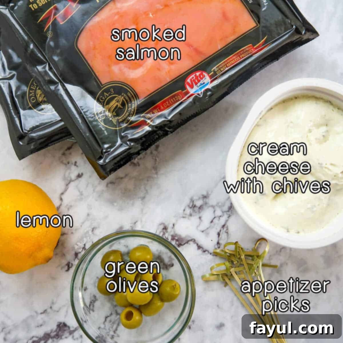 Overhead shot showcasing all the simple ingredients required for smoked salmon bites: smoked salmon slices, a tub of chive cream cheese, fresh lemons, whole green olives, and appetizer picks, all arranged on a pristine white surface.