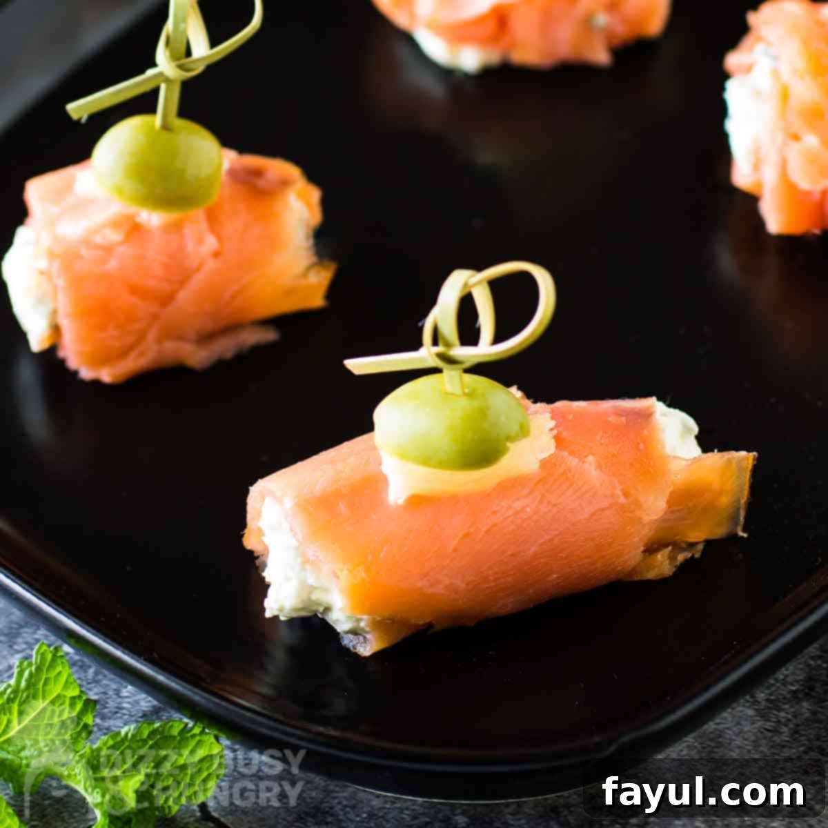 Overhead side view of an elegant platter of smoked salmon and cream cheese bites, garnished with fresh herbs, arranged on a black plate, highlighting their unique and flavorful combination.