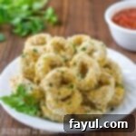 Side view of perfectly golden baked calamari rings, lightly seasoned with herbs, served on a crisp white plate with a side of dipping sauce in the background.