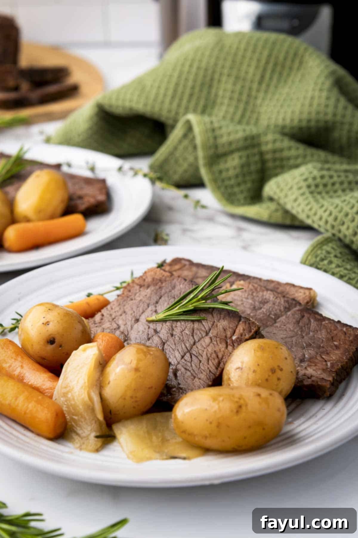 Side shot of a perfectly cooked rump roast, surrounded by tender potatoes and carrots on a white plate, garnished with fresh rosemary. A green cloth is softly blurred in the background, hinting at rustic comfort.