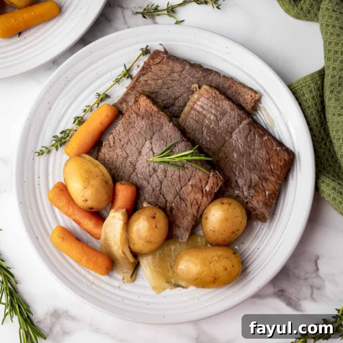 Overhead shot of a delicious rump roast, potatoes, and carrots on a white plate, beautifully garnished with fresh rosemary and a green cloth in the background, highlighting its tenderness.