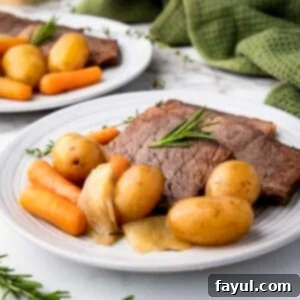 Side shot of rump roast, potatoes, and carrots on a white plate garnished with rosemary with a green cloth in the background.