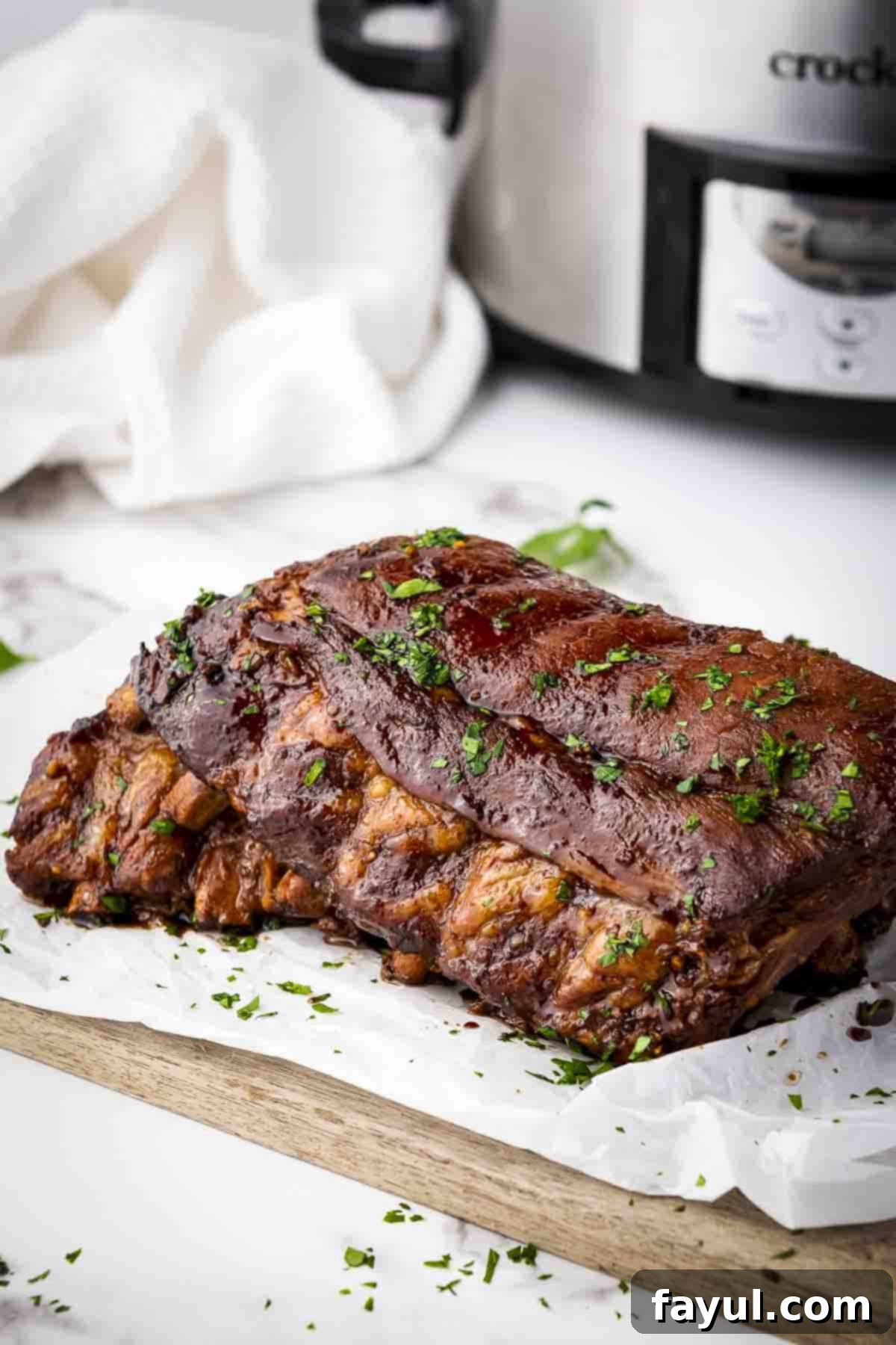 Side shot of multiple ribs garnished with parsley on a piece of butcher paper on a wooden cutting board, showcasing their sticky, glazed finish.