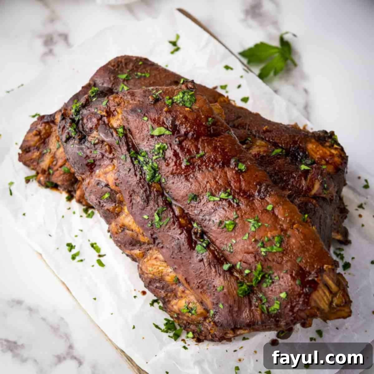 Overhead shot of multiple ribs garnished with parsley on a piece of butcher paper on a wooden cutting board, showing a perfectly glazed finish.