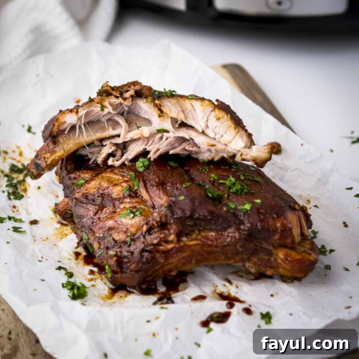 Side shot of multiple ribs garnished with parsley on a piece of butcher paper on a wooden cutting board, with a focus on the rich glaze.