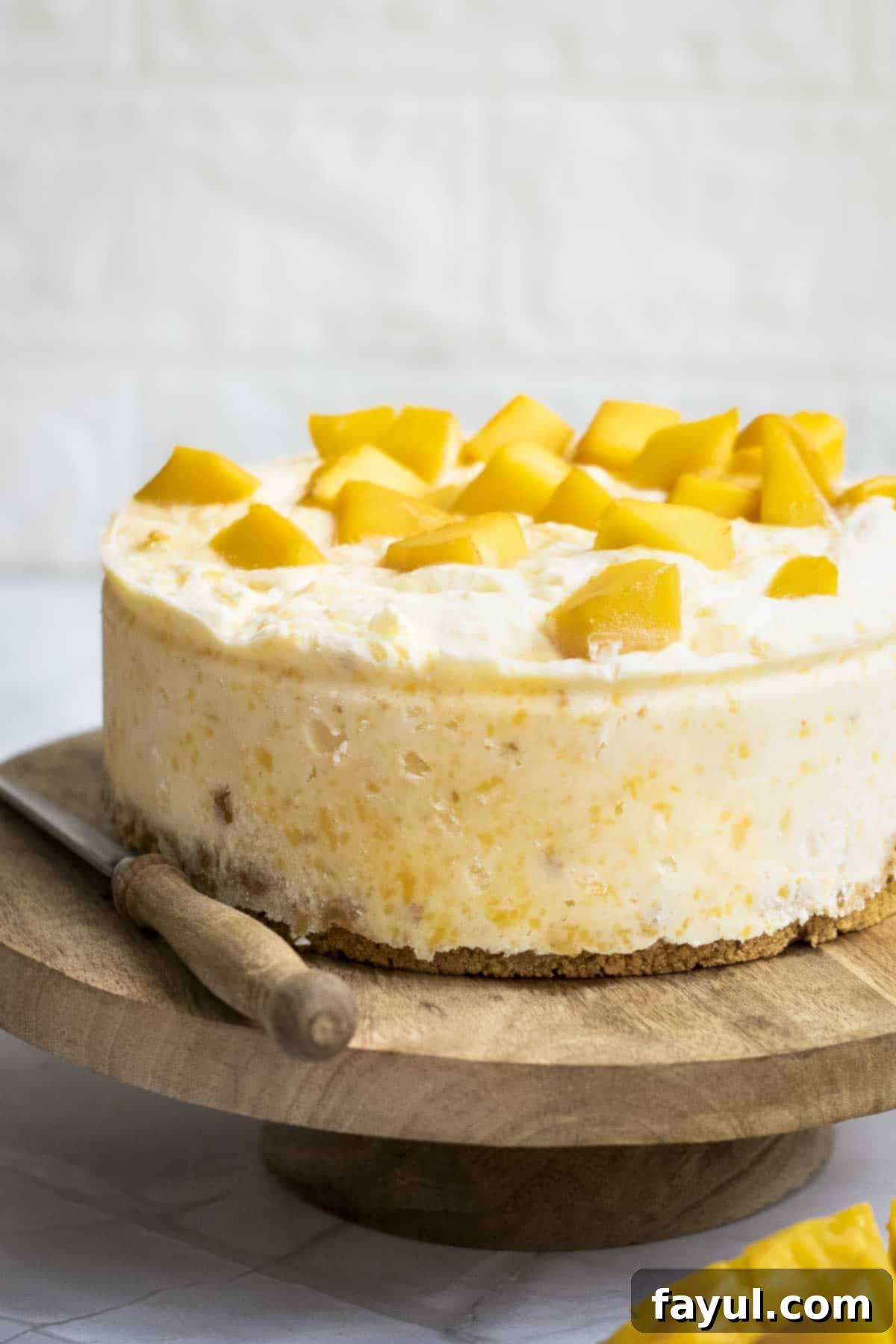 Velvet Mango No-Bake Delight 2 Side shot of the mango cheesecake on a raised wooden cake platter with a knife and mango on the side.