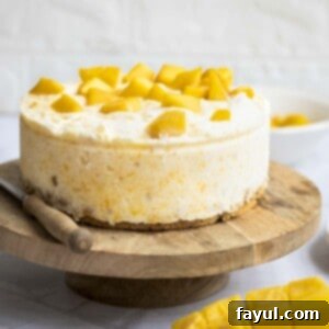 Velvet Mango No-Bake Delight 11 Side shot of the mango cheesecake on a raised wooden cake platter with a knife and mango on the side.