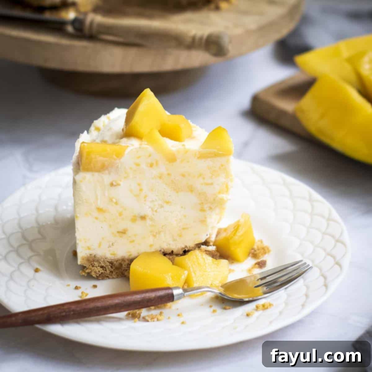 Velvet Mango No-Bake Delight 10 Side close up shot of a slice of mango cheesecake on a white scalloped plate with a fork on the side.