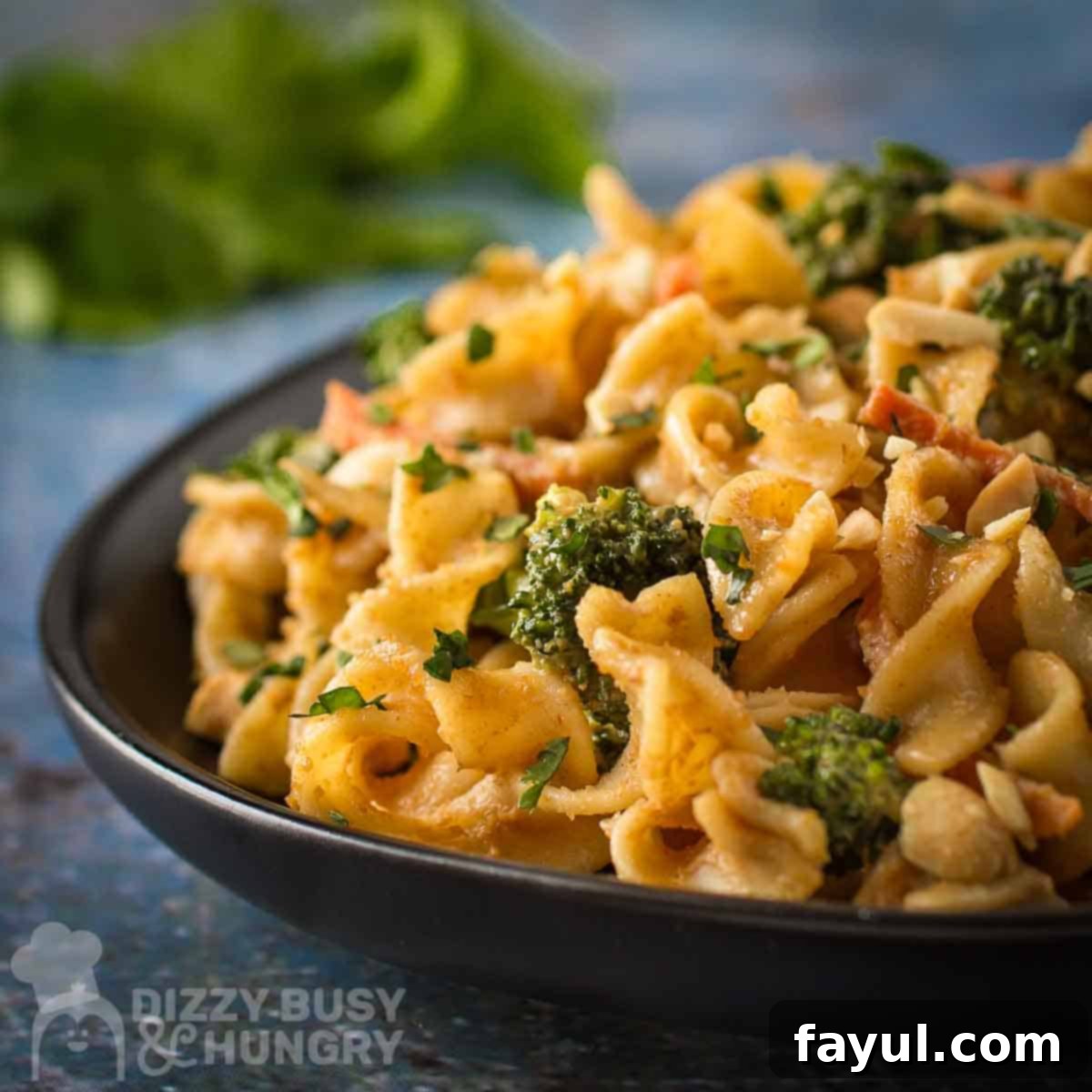 Side close up shot of noodles and broccoli garnished with chopped peanuts on a black plate with herbs on the side.