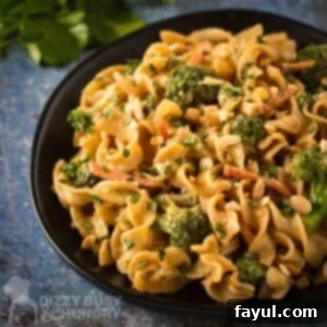 Close up angled shot of noodles and broccoli garnished with chopped peanuts on a black plate with herbs on the side.
