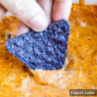 Hand dipping chip into chili cheese dip.