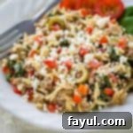 Side angled view of a serving of ground beef orzo pasta in a white bowl, with a fork resting on the side, ready to be enjoyed.