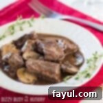 Side shot of Crock Pot Beef and Mushrooms in a white bowl, elegantly garnished with fresh herbs, resting on a red cloth with a fork on the side.