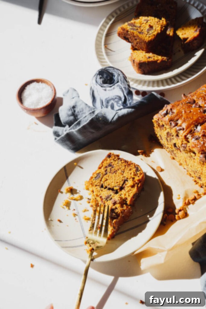 Close-up of a rustic slice of pumpkin chocolate chip bread on a wooden surface, showing the moist texture and melted chocolate chips.