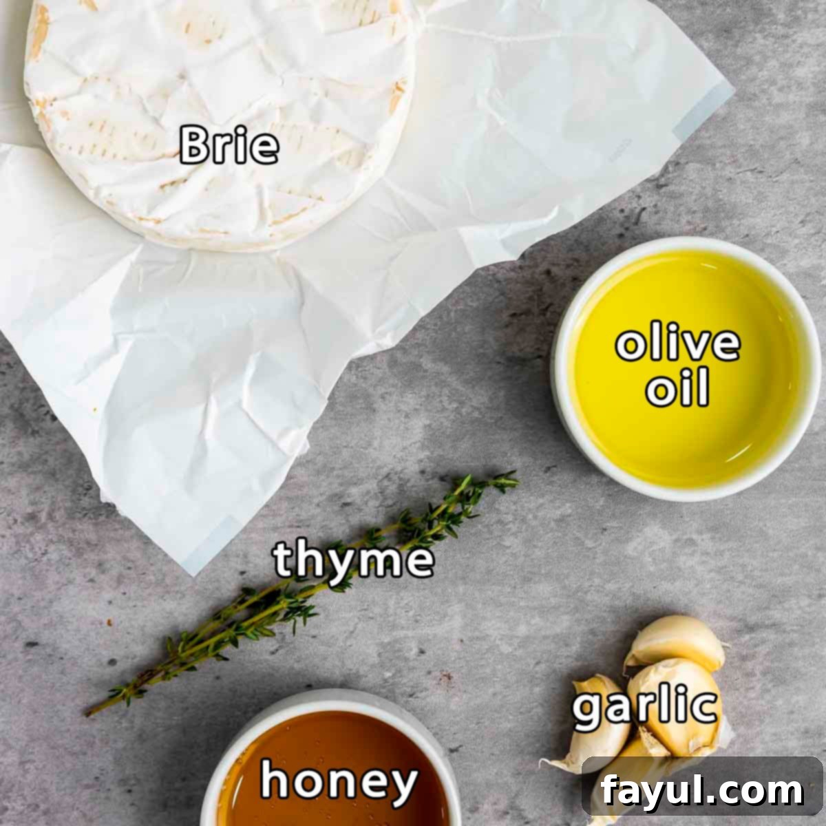 Overhead shot of fresh ingredients for baked brie with honey: a wheel of brie, fresh garlic cloves, a jar of honey, and fresh thyme sprigs neatly arranged.