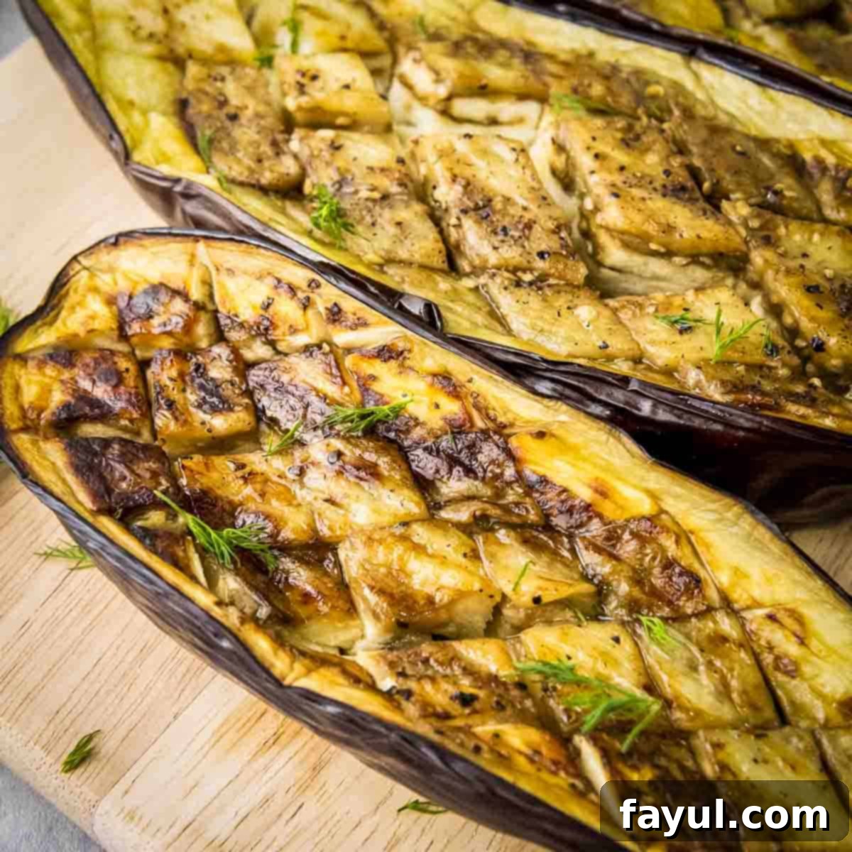Overhead close up shot of two slices of roasted eggplant garnished with fresh dill on a wooden cutting board, highlighting the rich caramelization and tender texture. A small bowl of garlic dill yogurt sauce is out of focus in the background.