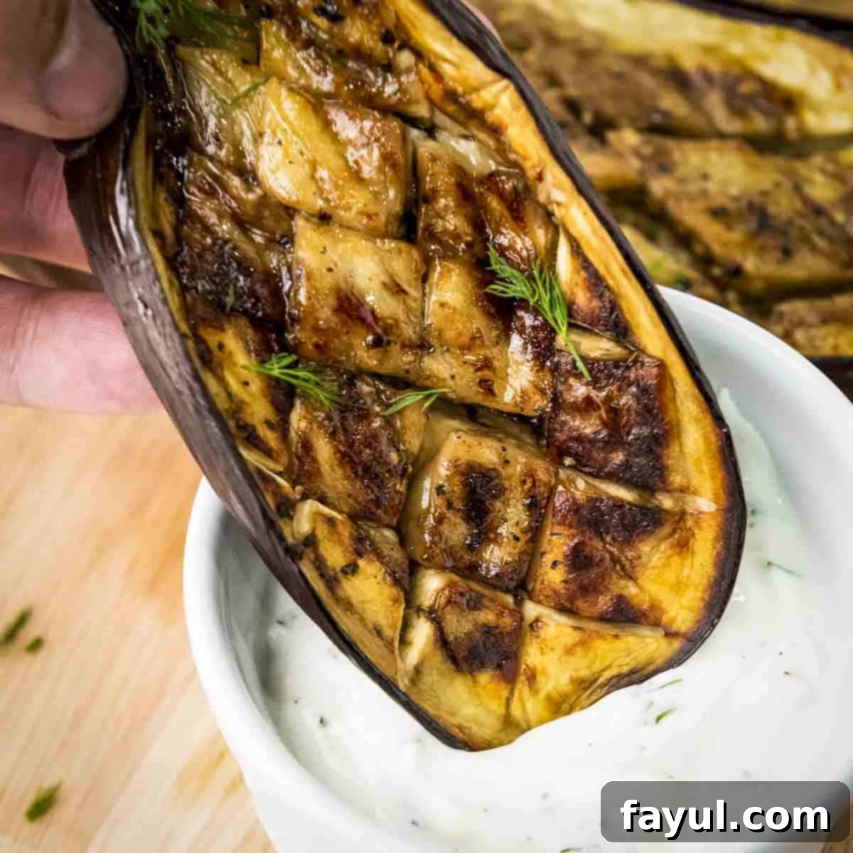 Side shot of a slice of roasted eggplant garnished with fresh dill being dipped into garlic dill yogurt sauce, showcasing the creamy texture and vibrant color.