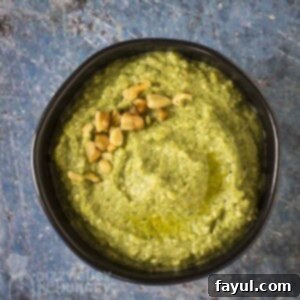 Overhead shot of zucchini pesto garnished with chopped walnuts in a black bowl on a blue marble surface.