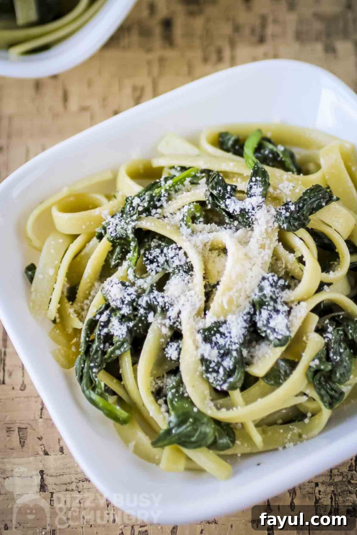 Overhead close up shot of fettuccine with spinach and parmesan in a white bowl on a wooden table. Delicious and easy spinach pasta.