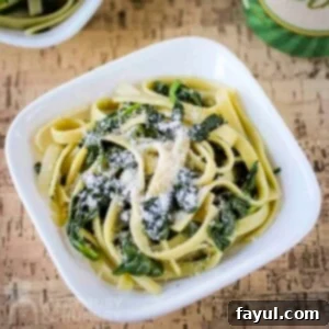 Overhead shot of fettuccine with spinach and parmesan in a white bowl on a wooden table.