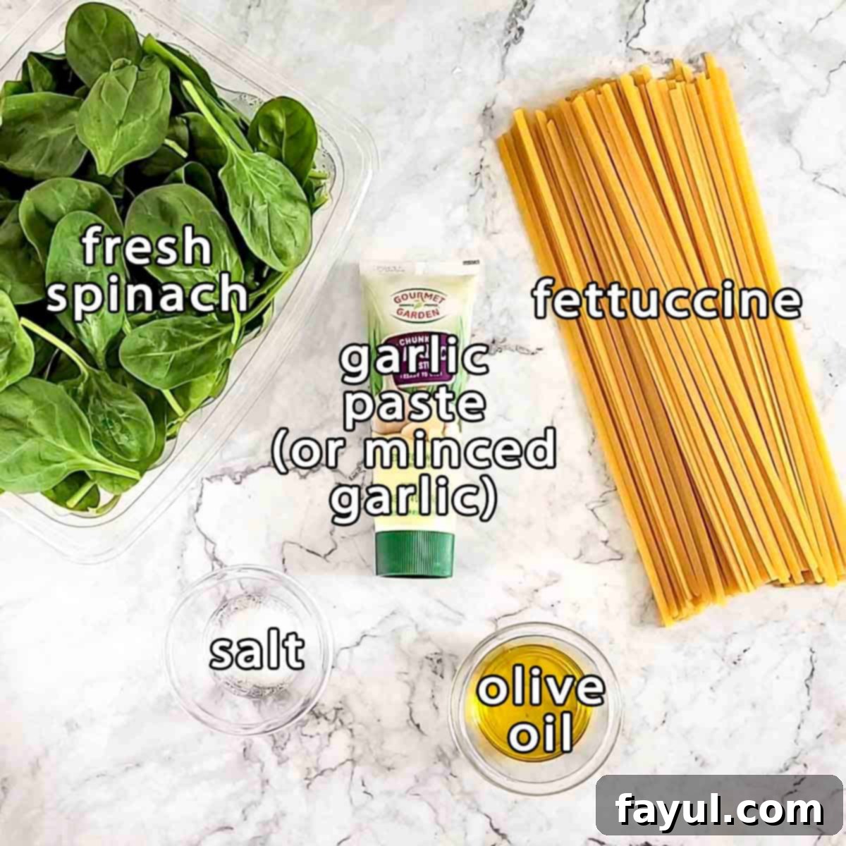 Overhead shot of fresh ingredients: bundles of fresh spinach, dry fettuccine pasta, a bowl of minced garlic (or garlic paste), coarse salt, and a bottle of olive oil, ready for cooking.