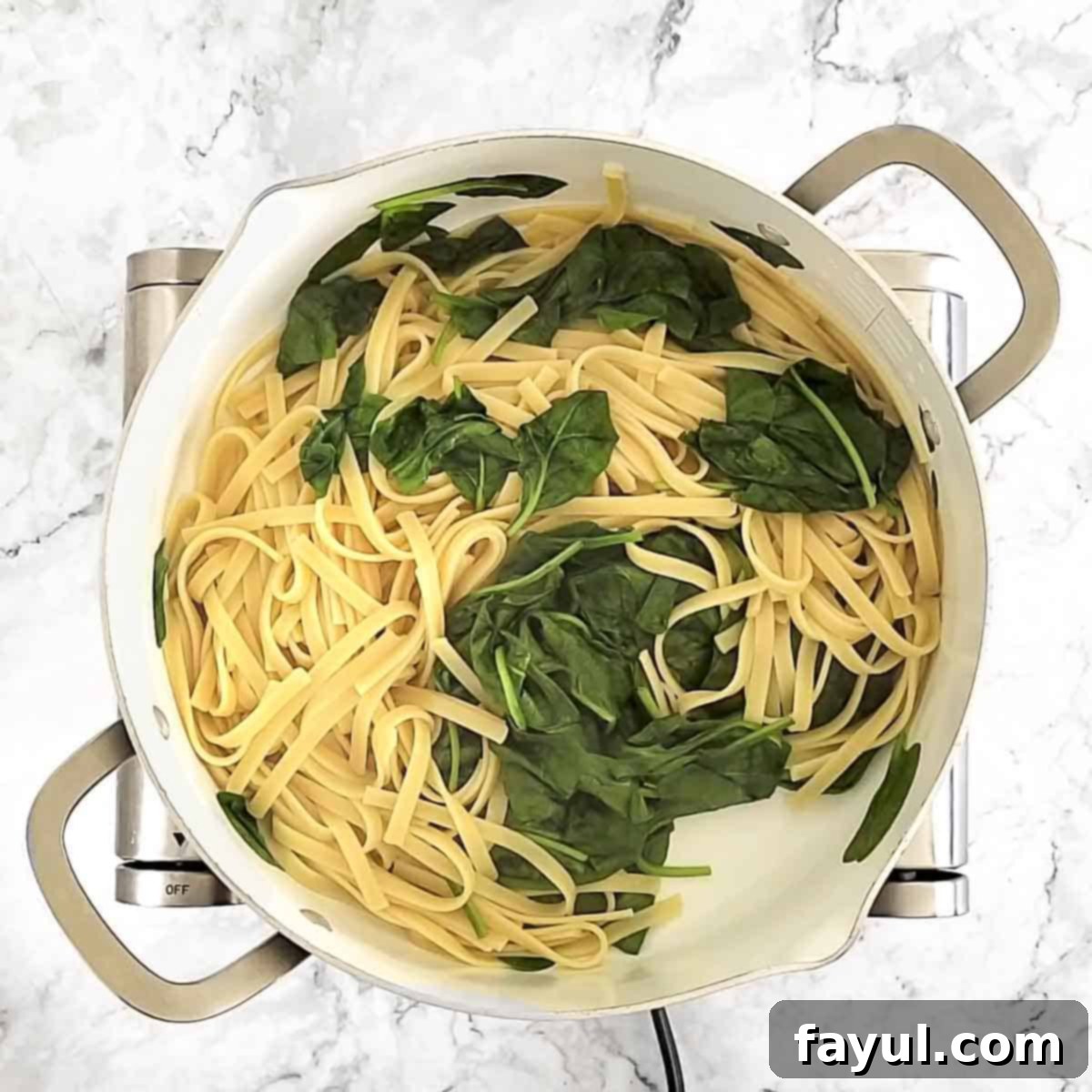 Overhead view of process shot 2 - Fresh spinach being stirred into the boiling pasta water to wilt just before draining the fettuccine.