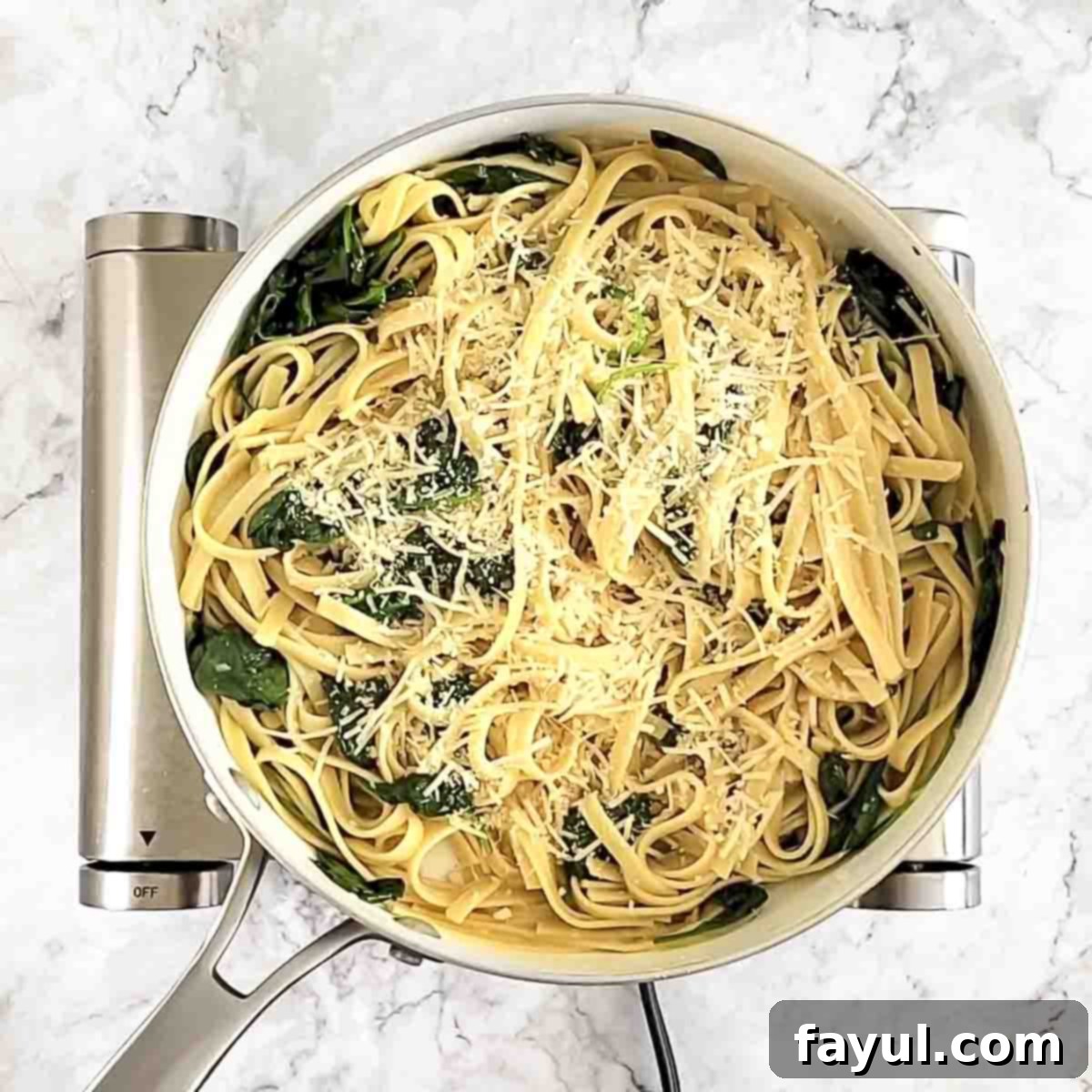 Overhead view of process shot 5 - A generous sprinkle of grated Parmesan cheese over the finished spinach fettuccine in a white bowl, ready to be served.