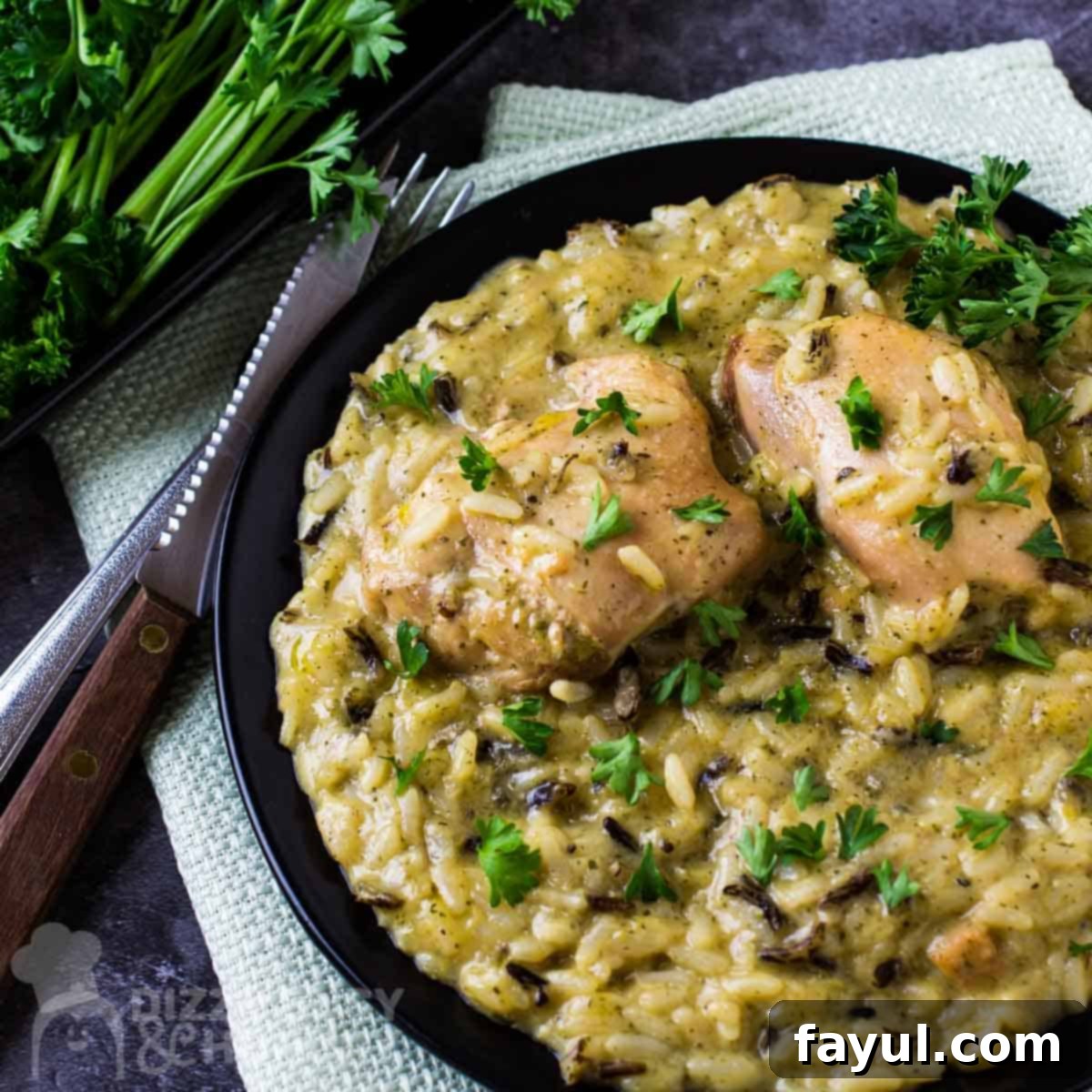 Overhead shot of slow cooker chicken and rice sprinkled with herbs on a black plate with a fork and knife on the side.
