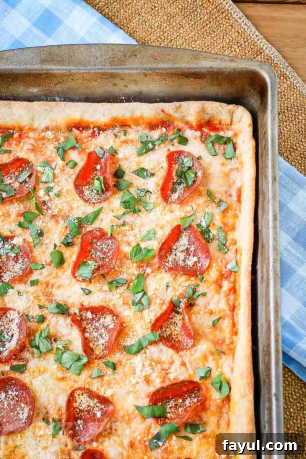 Overhead of full pan pizza garnished with parmesan cheese and basil on a blue plaid cloth.