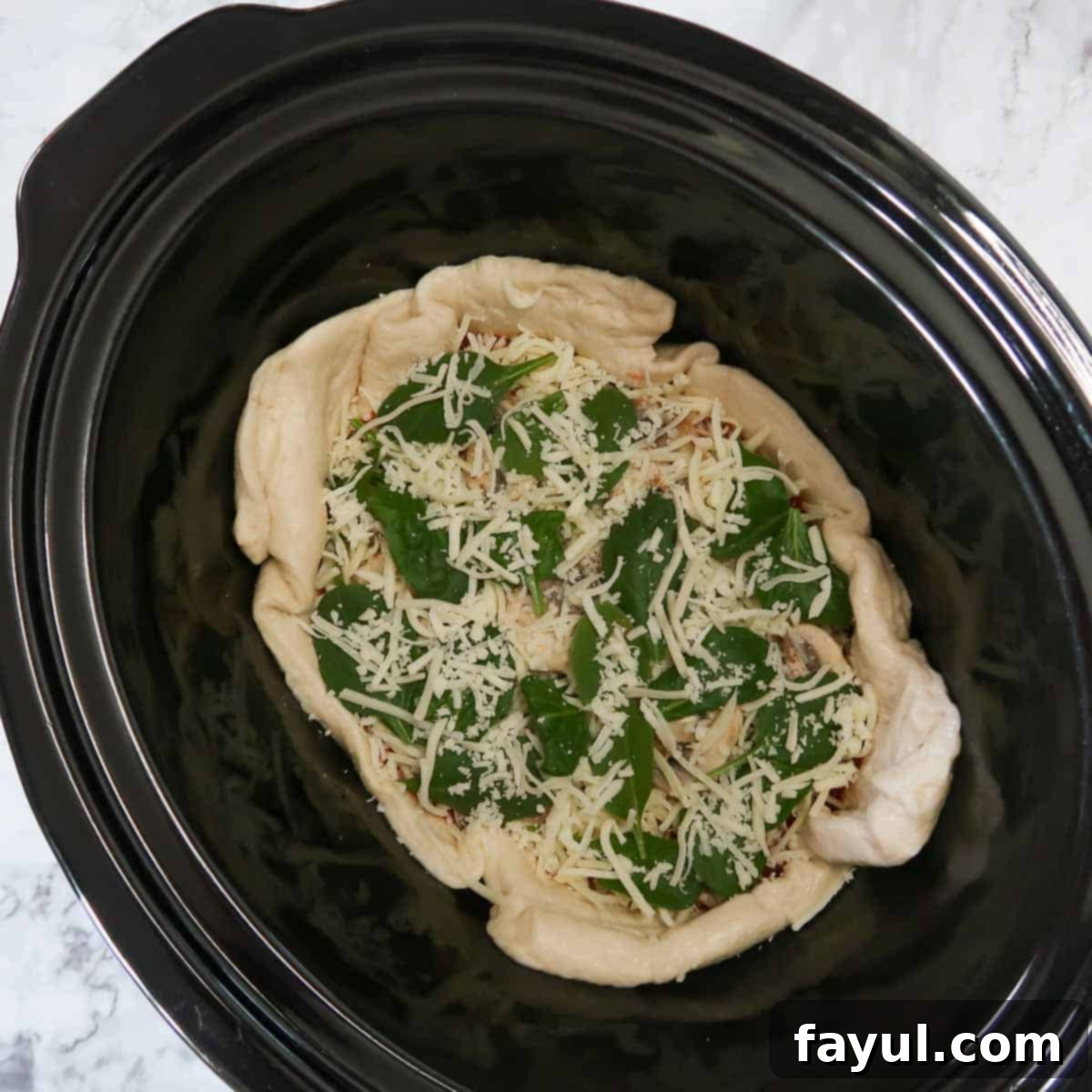 Raw pizza dough and toppings tucked into the bottom of a black crockpot before being cooked.